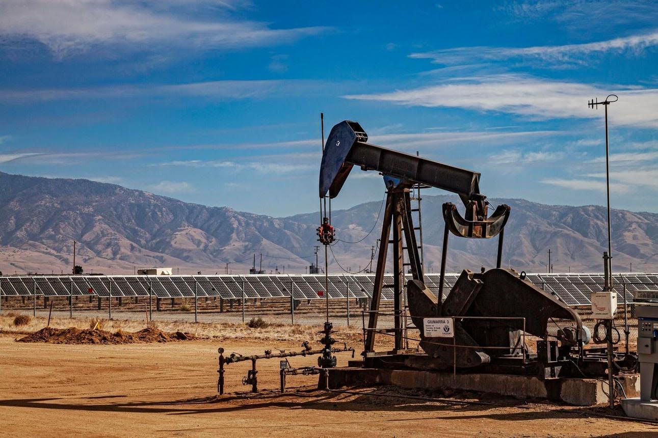An operating oil pumpjack and a utility-scale solar array coexisting in the same West Texas landscape