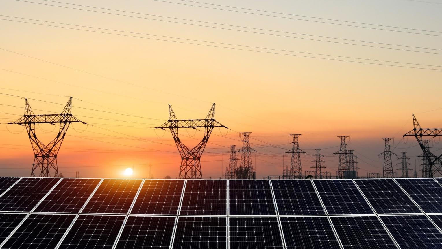 Solar array and high-voltage transmission towers sharing the same landscape at sunset